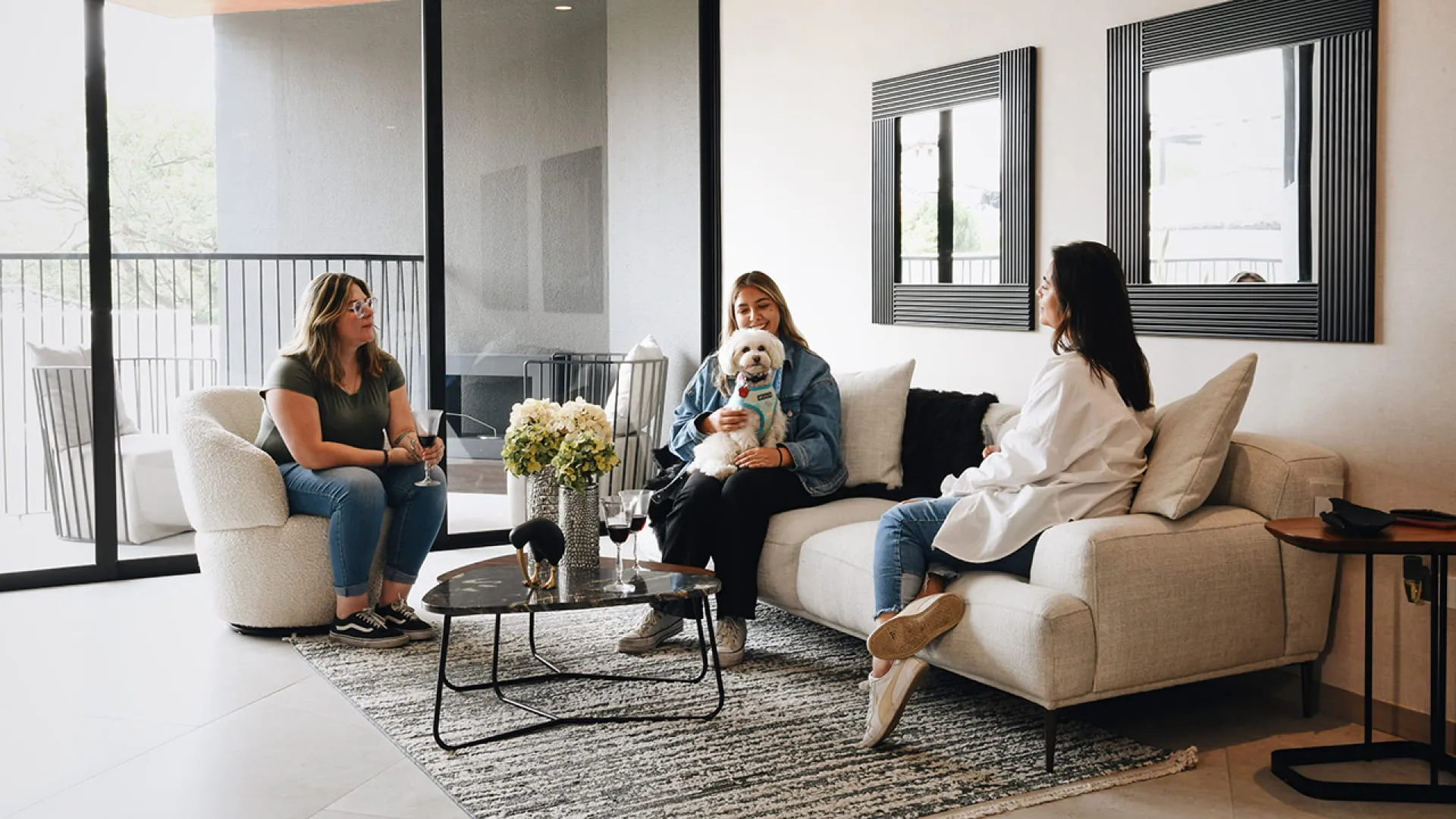 3 mujeres platicando en la sala mientras una carga un perro blanco